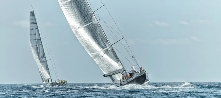 Zwei Hochseeyachten mit gesetzten Segeln in Schräglage auf hellblauem Meer