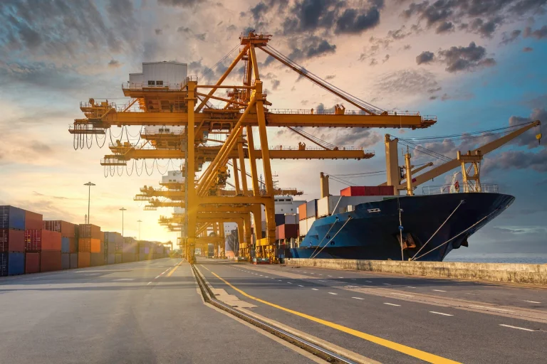 Containerhafen bei Sonnenuntergang mit gelben Kränen und einem Containerschiff