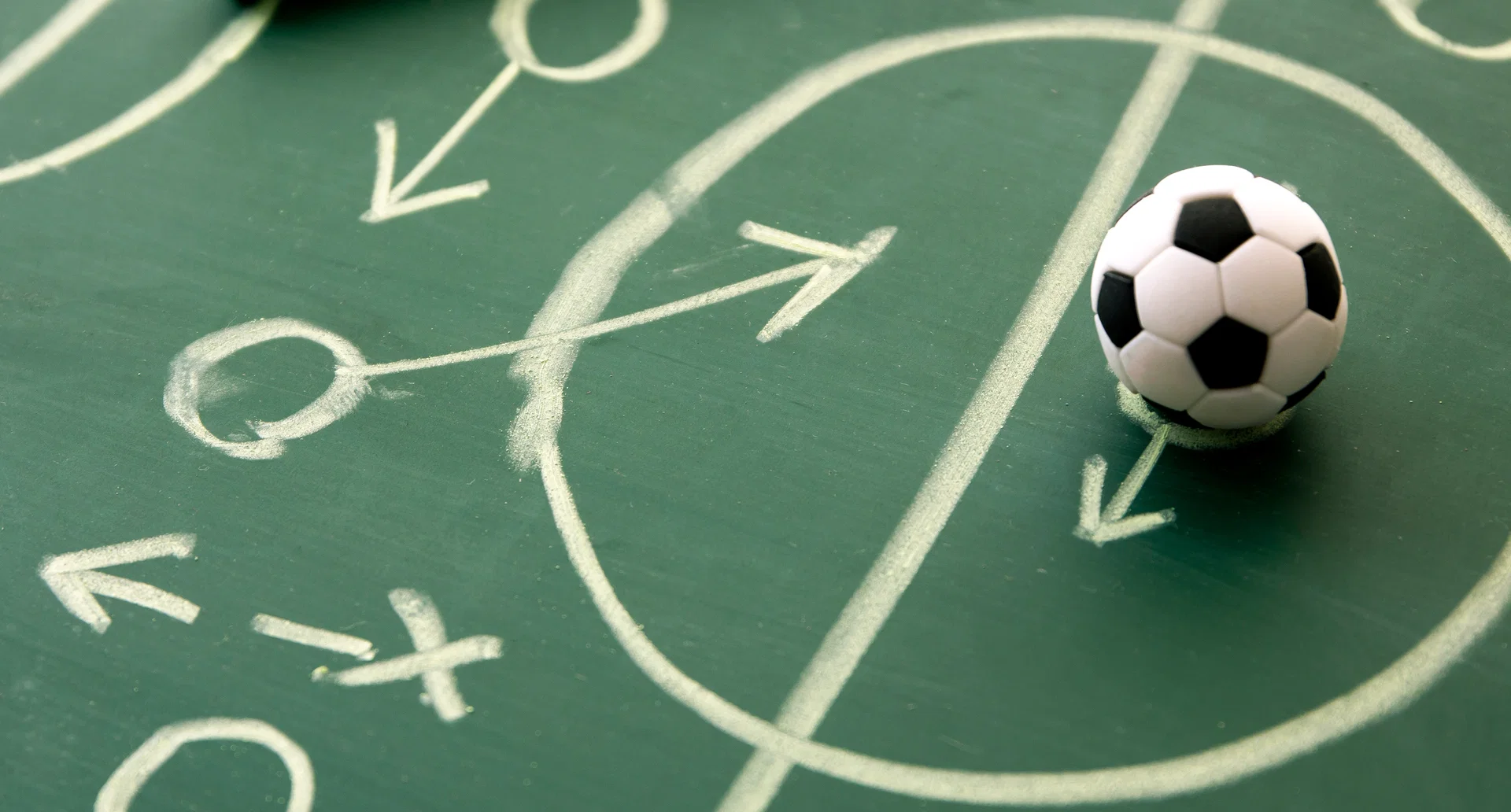 Grüne Taktiktafel mit Kreidepfeilen und Kreisen, davor ein kleiner Fussball