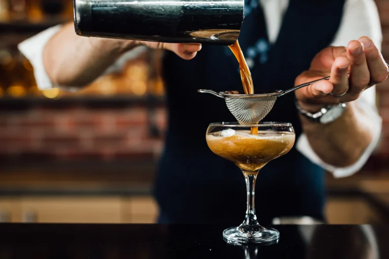 Barkeeper giesst einen Cocktail aus dem Shaker durch ein Sieb in eine Cocktailschale