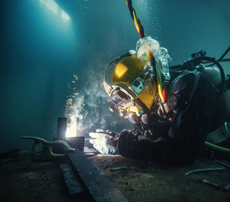 Industrietaucher mit gelbem Helm schweisst unter Wasser, Funken und Luftblasen