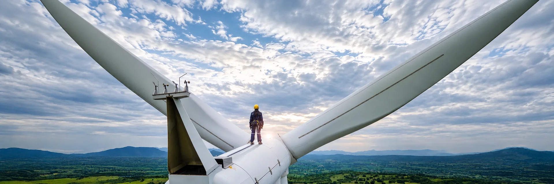 Techniker steht auf der Gondel einer Windkraftanlage über einer weiten Landschaft