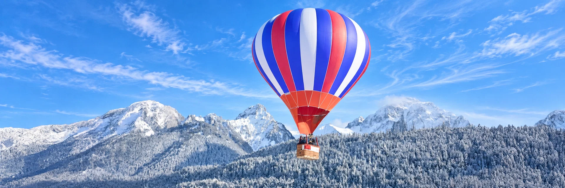 Heissluftballon schwebt vor verschneiten Berggipfeln